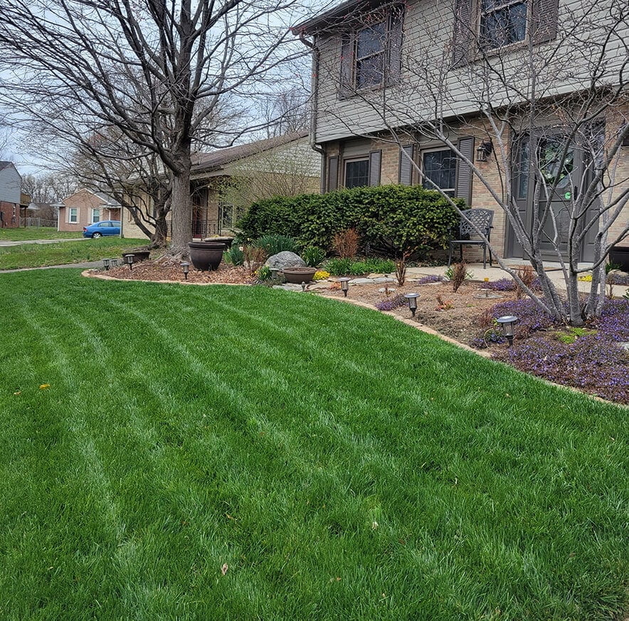 A well-manicured lawn in front of a two-story suburban house with a landscaped garden.