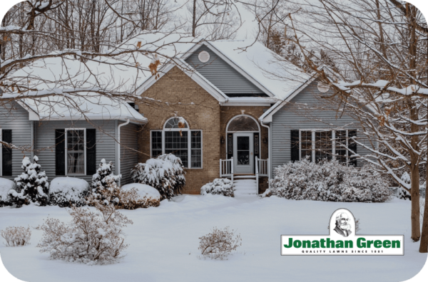 Sentence with product name: A snow-covered house and landscape with a Jonathan Green eGift Card lawn sign in the foreground.