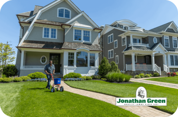 Man fertilizing lawn in front of a large suburban home with Jonathan Green eGift Cards.