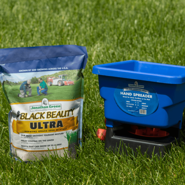 A Jonathan Green Black Beauty Ultra grass seed starter kit featuring a bag of Jonathan Green Black Beauty Ultra grass seed next to a blue hand spreader on grass.