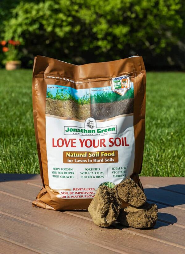 A bag of jonathan green "love your soil" natural soil food for lawns, part of the Fall Lawn Care Bundle, is displayed on a wooden surface with a clump of soil in front.