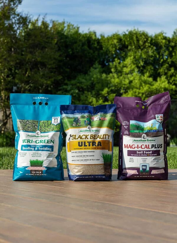 Three bags of Grass Seed & Fertilizer Bundle for Alkaline Soil, displayed on a wooden surface outdoors.