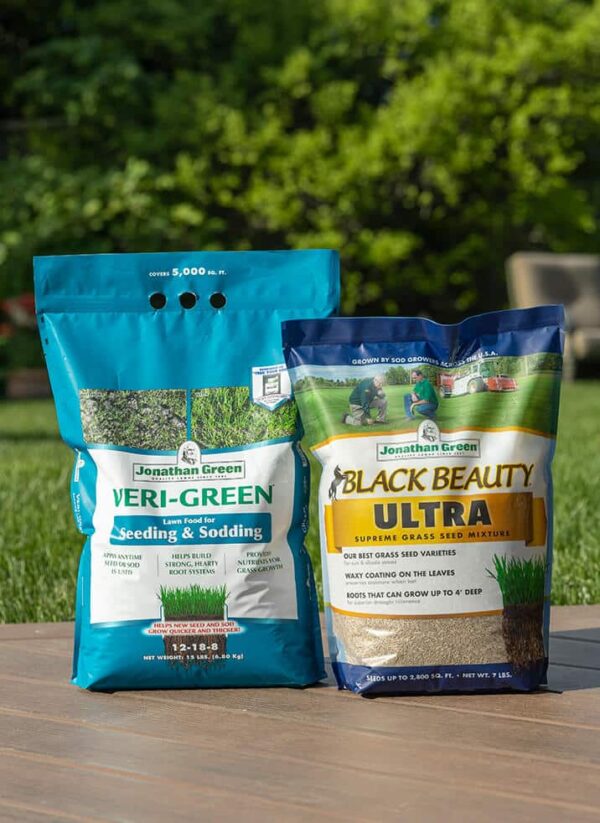 Two bags of Grass Seed & Fertilizer Bundle mixtures placed on a wooden table outdoors.