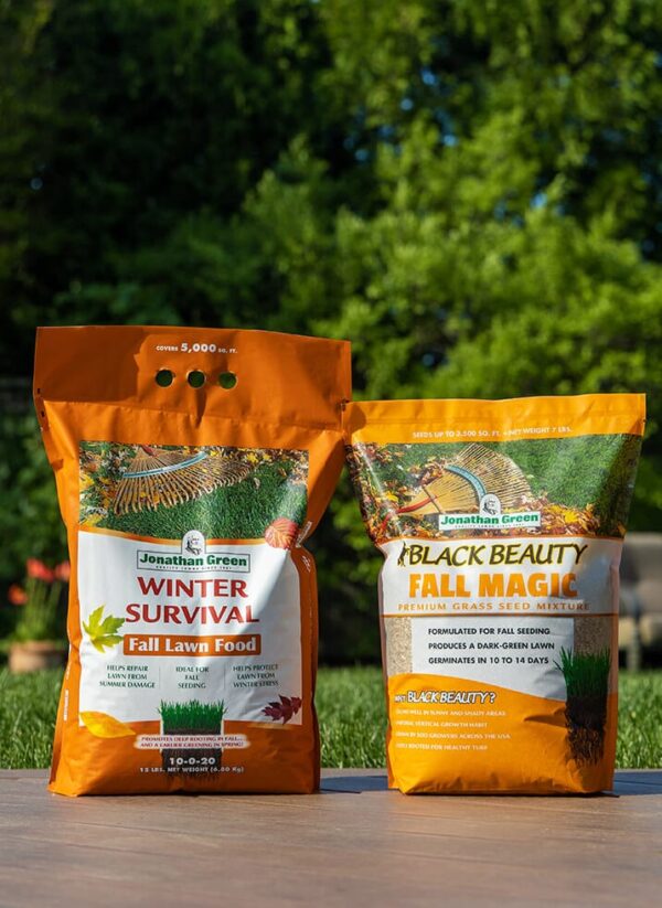 Sentence with replaced product name: Two bags of Jonathan Green lawn fertilizer, "Winter Survival" and "Black Beauty Fall Magic," part of the Fall Lawn Care Bundle, standing on pavement with greenery in the background.