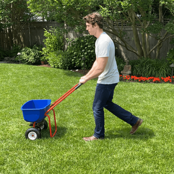 A man pushing a Lawn Starter Kit spreader across a grassy yard.
