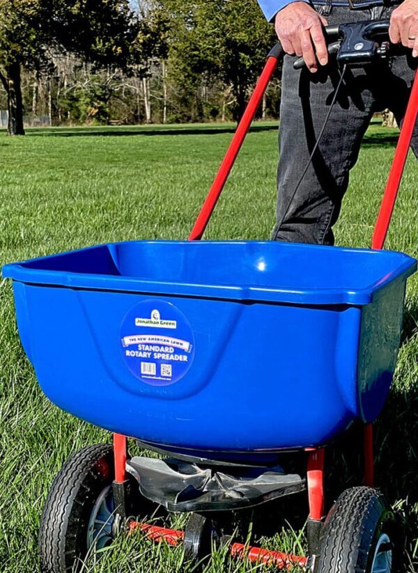 A person operating a blue rotary spreader from a Lawn Starter Kit on a grassy field.