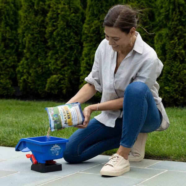 A woman pouring fertilizer into a Jonathan Green Hand Spreader on a garden path.
